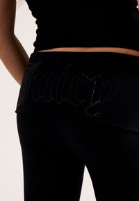 Leggings neri con una texture liscia presentano un logo "Juicy" abbellito da strass sulla vita, offrendo un design aderente.