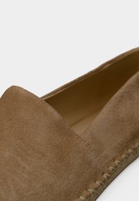 Κοντινή λήψη ενός ταμπά μοκασίνι από σουέντ με εμφανείς ραφές κατά μήκος της σόλας και λείο εσωτερικό επένδυση.