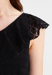 Svart spetsklänning med volangärmar och blommönster, med en strukturerad yta och figurnära design.