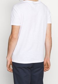 Biała koszulka z bawełny z klasycznym okrągłym dekoltem, krótkimi rękawami i luźnym krojem. Charakteryzuje się minimalną teksturą oraz detalem metki po boku.