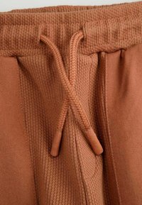 Spodnie dresowe w kolorze rdzy z teksturowanym pasem i plecionym sznurkiem. Kieszenie boczne wkomponowane w gładki design.