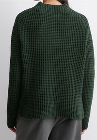 Zielony sweter dziany z teksturowanym wzorem, długimi rękawami i okrągłym dekoltem, o luźnym kroju i nieco dłuższym tylnym brzegu.