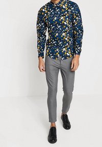 Mörkblå långärmad skjorta med ett färgglatt blommönster, i kombination med slim-fit grå byxor och svarta sneakers. Lämplig för vardagsbruk.