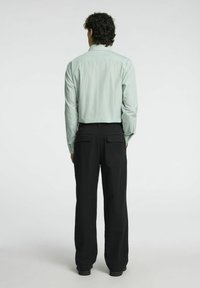 Mėtų žalios spalvos juostuota ilgomis rankovėmis marškiniai su pritaikytu siluetu, derinami su juodomis kelnėmis, turinčiomis dvi užpakalines kišenes, matoma nuo nugaros.