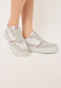 Sneakers z połączeniem białej skóry i jasnoszarego zamszu, z różowymi akcentami, teksturowaną podeszwą i perforowanymi detalami.