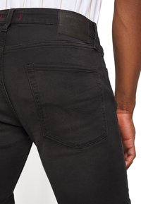 Jeans in denim nero con vestibilità slim, dotati di una tasca posteriore con cucitura curva e un'etichetta in pelle nera sul cinturino.