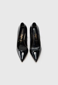 Pantofi cu toc înalt din piele lacuită neagră, cu vârf ascuțit și textură netedă, având un logo auriu pe branț.
