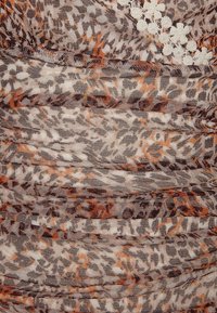 Tissu transparent avec un motif superposé d’imprimé léopard en tons bruns, oranges et beige, agrémenté de petites applications florales blanches.