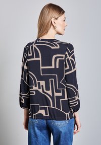 Haut marine avec un motif abstrait beige, manches 3/4 et col rond. Associé à un denim bleu clair, mettant en valeur une coupe décontractée.