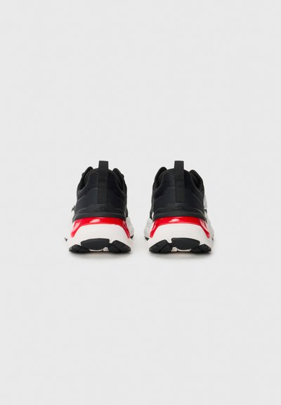 Black athletic shoes with a round toe, textured mesh upper, red accents on the heel, and a white sole featuring a black tread pattern.