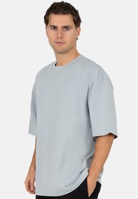 Lichtgrijs oversized T-shirt met korte mouwen. Heeft een ronde halslijn en een rechte zoom. Gladde stoftextuur zonder patronen.