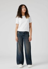 Balti trumpomis rankovėmis marškinėliai, derinami su tamsiai mėlynais plačiomis kojomis džinsais. Džinsai turi išblukusią apdirbimą, priekinės kišenės ir sagų užsegimą. Balti sportbačiai.