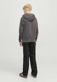 Siva kapuca sweatshirt, kombiniran s črnimi hlačami. Sweatshirt ima sproščen kroj in rebraste manšete, medtem ko imajo hlače raven kroj.
