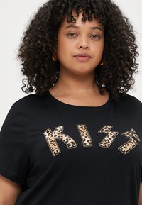 Μαύρη μπλούζα με κοντά μανίκια που φέρει το "KISS" σε μεγάλα γράμματα με λεοπαρ δέρμα και στρας. Έχει στρογγυλή λαιμόκοψη.