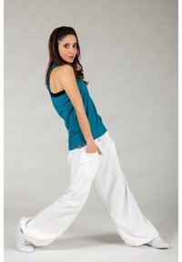 Turquoise tank top paired with white wide-leg trousers. Outfit features a relaxed design, with visible side pockets and a casual fit.