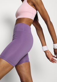 Violetti korkevyötäröiset pyöräilyshortsit, jotka on valmistettu joustavasta kankaasta. Ne ovat sileäpintaiset ja vartalonmyötäiset. Vyötäröllä saumaton resori.