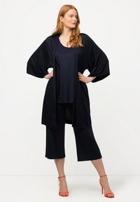 Námořnický modrý komplet zahrnující volný, splývavý kimono a zkrácené kalhoty, vyrobený z měkké tkaniny s hladkou texturou. Doplněný oranžovými podpatky.