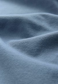 Blauwe katoenstof met een gladde, iets gestructureerde oppervlakte, met zachte plooien en lichte kreukels. Effen kleur zonder zichtbare patronen.