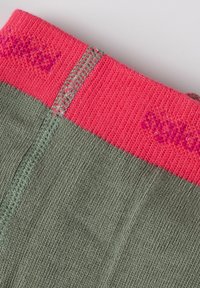 Tessuto verde testurizzato con polsino a coste rosa; presenta cuciture a contrasto e la parola "stgild" in rosa vicino al bordo superiore.