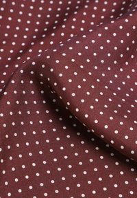Bordeaux stof met witte stippen, met een gladde textuur en subtiele glans, diagonaal gerangschikt over het oppervlak.