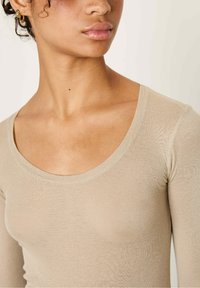 Beige long-sleeve top with a scoop neckline, ribbed texture, and soft fabric. Close-up view of the neck and shoulders, no visible patterns or details.