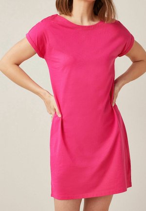 Woman wearing a bright pink short-sleeve, knee-length casual dress with hands resting on hips against a plain background.
