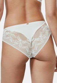 Lingerie blanche avec un mélange de tissu lisse et des bordures en dentelle florale. Présente une coupe taille basse et des détails délicats le long des bords.
