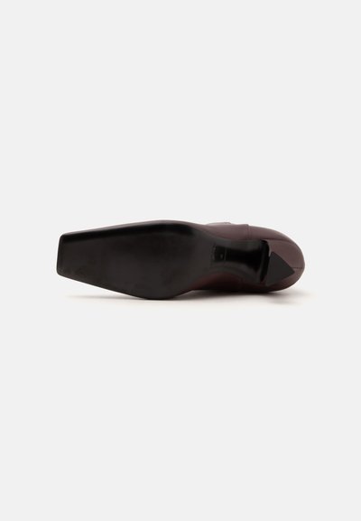 Chaussure en cuir marron vue depuis la semelle, montrant un bout carré et un talon noir sur fond blanc.