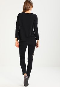 Svart långärmad topp som matchas med svarta jeans med blommig brodyr, tygtexturen ser mjuk ut, kroppsnära passform, med lediga skor.