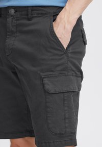 Pantaloni scurți cargo negri dintr-un amestec de bumbac, având buzunare laterale, un buzunar cu clapetă pe coapsă și închidere cu nasture. Textură netedă.