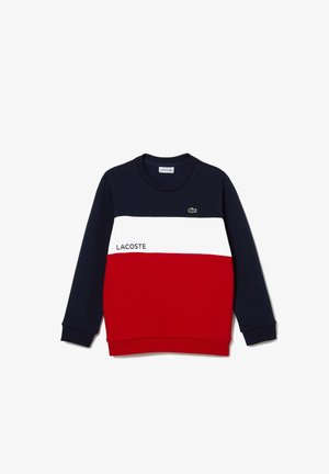 Pull Lacoste en color-block bleu marine, blanc et rouge avec col rond, manches longues, texte Lacoste et logo crocodile vert sur la poitrine.