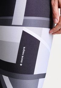 Leggings in bianco e nero con un motivo a fantasia, realizzati in un tessuto testurizzato e elastico. Presentano forme geometriche e includono l'etichetta del brand "Björk Borg."