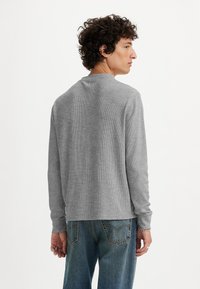 Camisa de manga larga de color gris con textura de canalé, de escote redondo, suave y de corte relajado, que se lleva con unos pantalones vaqueros azules. Sin patrones notable.