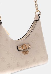 Beżowa torebka o fakturowanej powierzchni z wytłoczonymi wzorami logo, złotym okuciem i zamkiem błyskawicznym. Posiada łańcuszkowy pasek na ramię.