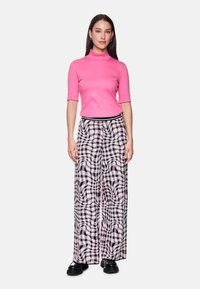 Fitted pink turtleneck top paired with wide-leg, patterned trousers in black and white, featuring a textured design and elastic waistband.
