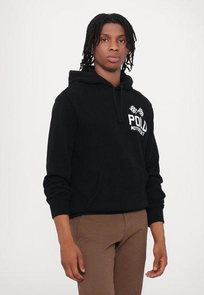 Melnā kapuce, izgatavota no mīksta kokvilnas, ar priekšējo kabatu, baltu logo tekstu "POLD MOTORSPORT" un šaha karoga akcentiem uz krūšu daļas.