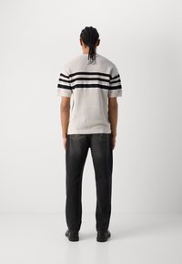 Texturiertes, beigefarbenes Strickpullover mit schwarzen horizontalen Streifen; kombiniert mit lockeren schwarzen Jeans und schwarzen Schuhen. Ansicht von hinten.