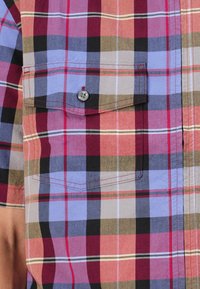 Short-sleeve plaid shirt featuring multi-colored squares in red, blue, and beige; includes a chest pocket with a button detail.