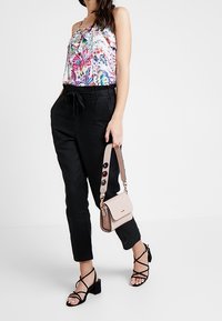 Top sin mangas con estampado floral, pantalones ajustados negros, sandalias negras con tiras y un pequeño bolso rosa con asa decorativa.