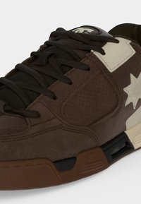 Baskets marron et noir avec lacets noirs, étoile crème et détails en patch, et une semelle épaisse marron et noire.