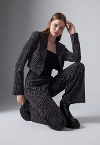 Zebra vzor v černé a stříbrné barvě, s blazrem a širokými kalhotami, doplněno robustními černými platformovými botami. Hladká textura s precizním střihem.