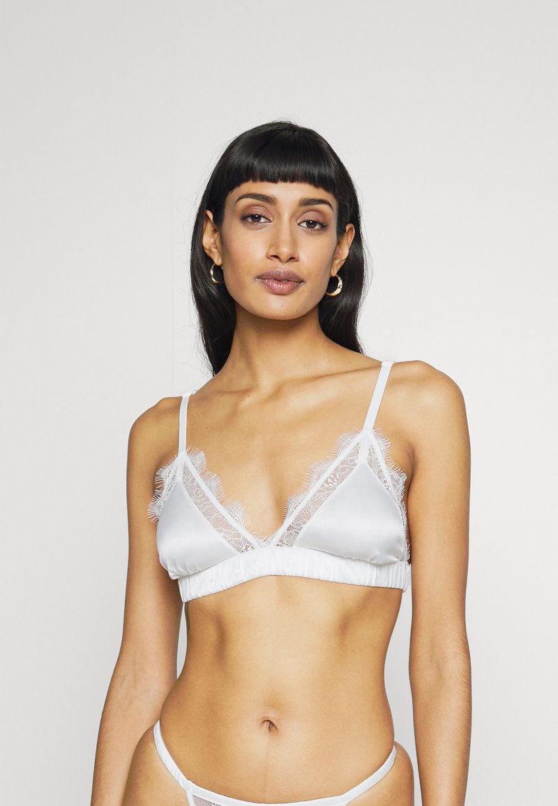 Bralette branco de cetim com acabamento em renda, apresentando uma forma triangular e finas alças ajustáveis. Textura suave, design simples e detalhes delicados.