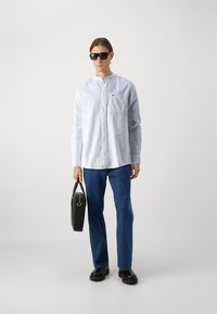 Camisa de manga larga azul clarito con botones, vaqueros rectos azul oscuro, gafas de sol negras y un bolso liso y oscuro con un asa corta. Calzado negro.