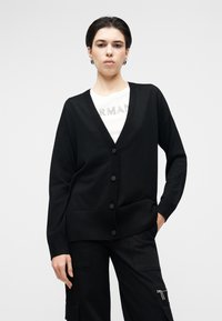 Cardigã preto com decote em V, fecho de botões e bolsos frontais; feito de um tecido de malha macio com punhos e barra canelados.