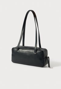 Μαύρη δερμάτινη τσάντα χειρός με ορθογώνιο σχήμα, απαλό υλικό, διπλούς ιμάντες ώμου και ασημένιο φερμουάρ. Διαθέτει διακοσμητικό φούντα.