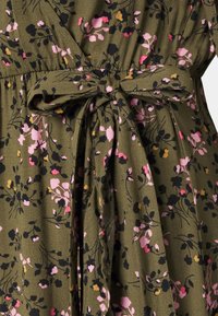 Vestido floral em tecido de verde oliva escuro com flores rosas, pretas e amarelas; detalhe de cintura atada e textura suave.