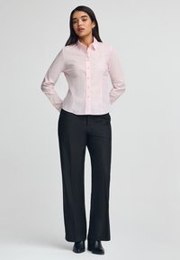 Camicia button-up rosa chiaro a maniche lunghe con un design aderente; indossata con pantaloni neri a gamba dritta e stivaletti. Finitura in tessuto liscia.