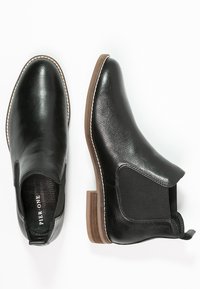Stivali Chelsea neri con finitura in pelle texturizzata, pannelli laterali elasticizzati e tacco impilato marrone. Cuciture bianche delineano la suola.