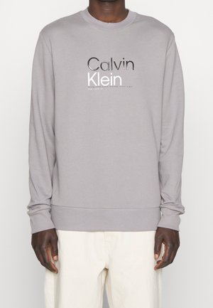 Světlounce šedá mikina z měkké látky, s kulatým výstřihem a žebrovanými manžetami. Velké logo Calvin Klein potisknuté černobíle.
