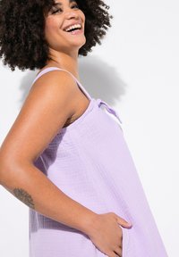Lavendelfarbenes ärmelloses Kleid aus leichtem, strukturiertem Stoff. Mit verstellbaren Trägern und seitlichen Taschen. Sanfter Fall, lässige Passform.